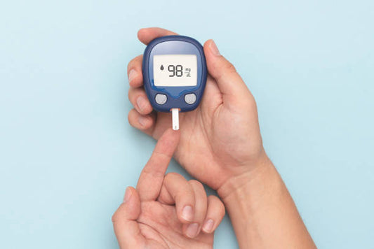 Person using digital blood glucose meter to test blood sugar level via fingertip on blue background