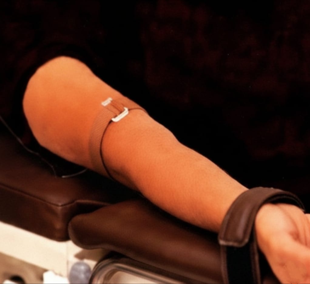 Close-up of a person's arm with a brown sleeve and strap on a dark background